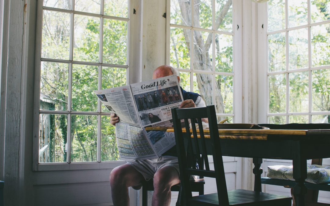 image of an older man reading a newspaper in a large room by himself