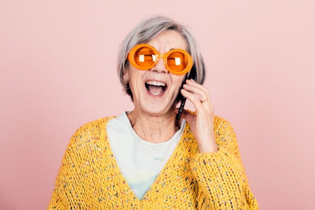 funky lady laughing while on the phone. she is wearing a yellow sweater and bright orange sunglasses
