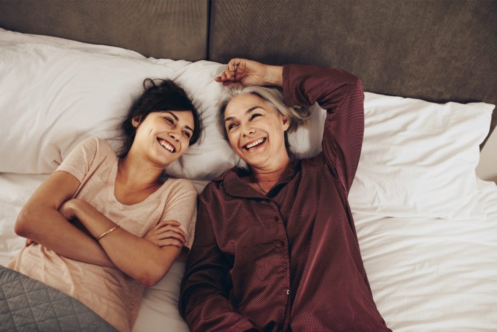 Mother and daughter laying on bed, relaxing, visiting and smiling. Let family visit and call you to prevent abusive caregiver situations