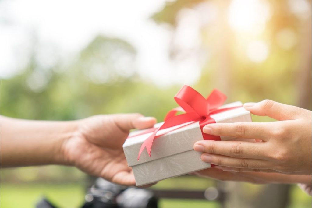 Close up of two hands giving a gift box with a red bow on it. 