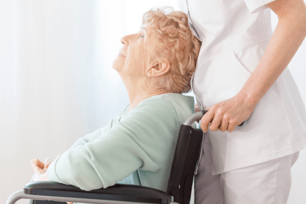 Wheelchair bound woman looking up at a nurse in white while at a nursing home for long-term care