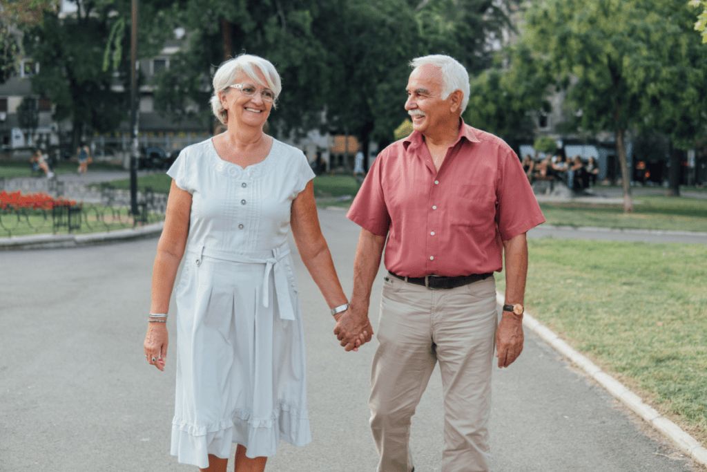 Middle-aged couple walking together hand in hand through a park. They are smiling. They look like a cute couple. 