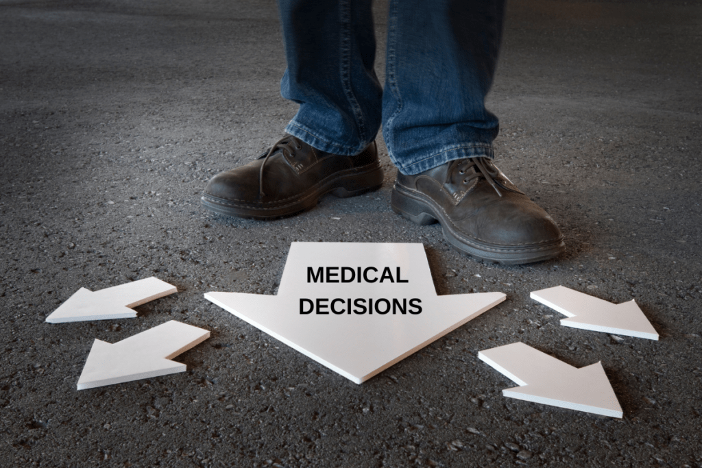 close up of a person wearing leather shoes and blue jeans. They are standing on asphalt in front of arrows that point in several directions. The largest arrow says "Medical Decisions"