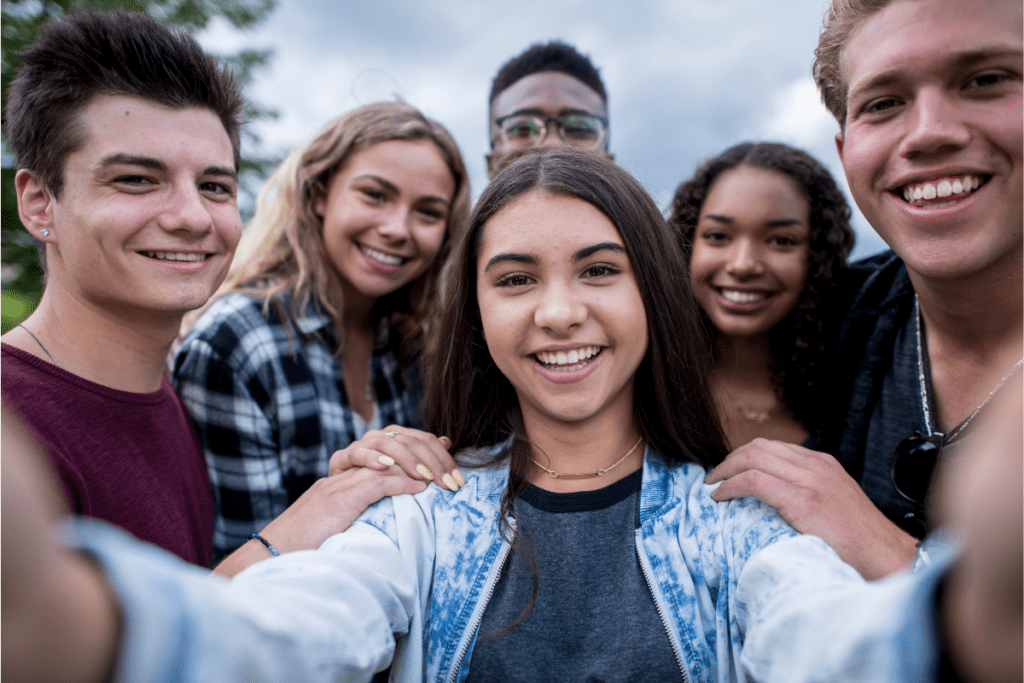 6 college students gathering in front of a cell phone to take a group photo. They are all smiling