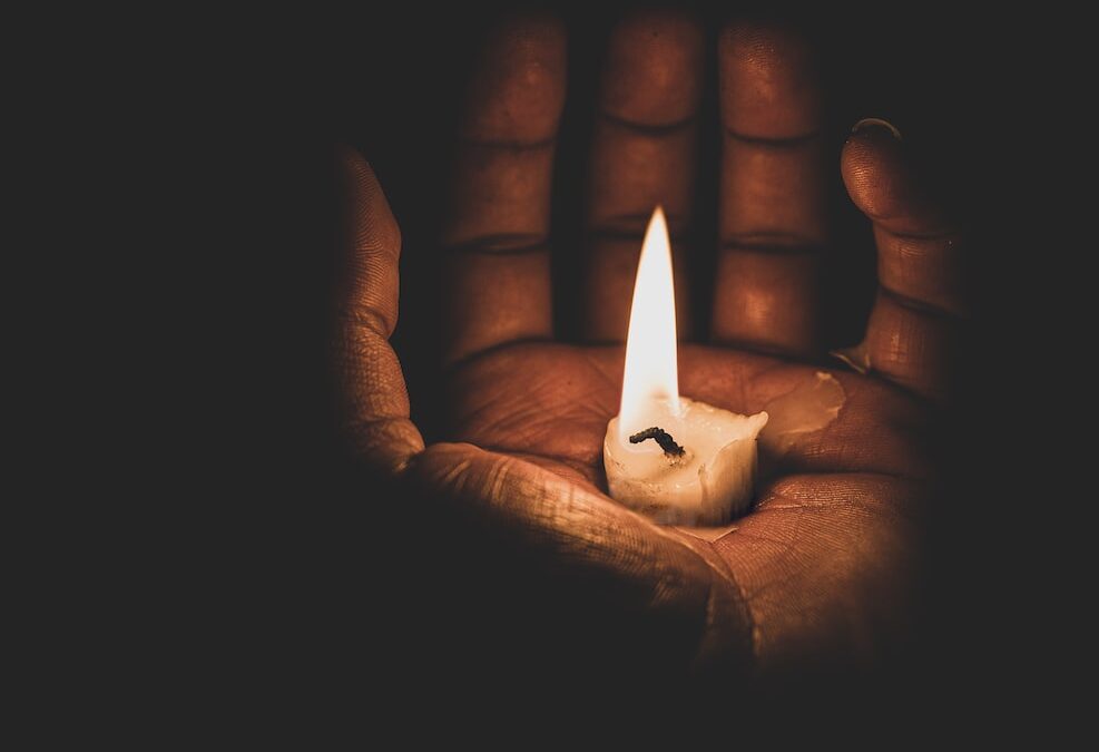 A nearly-spent candle in an open hand, illustrating the transition of death